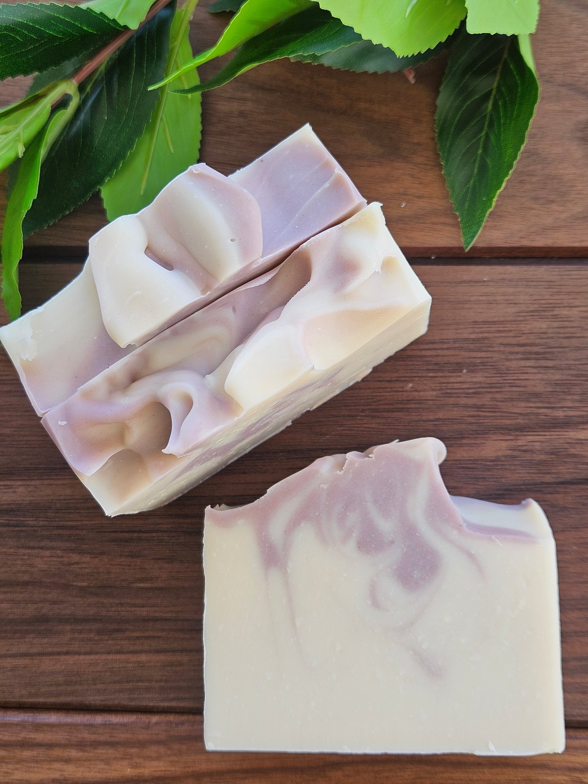Three bars of soap with a marbled design on a wooden surface, surrounded by green leaves.
