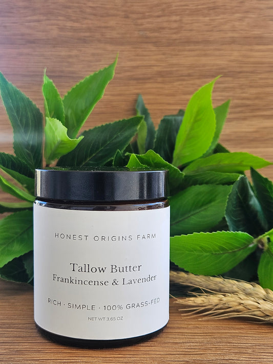 Jar of tallow butter labeled 'Frankincense and Lavender' on wood table with greenery