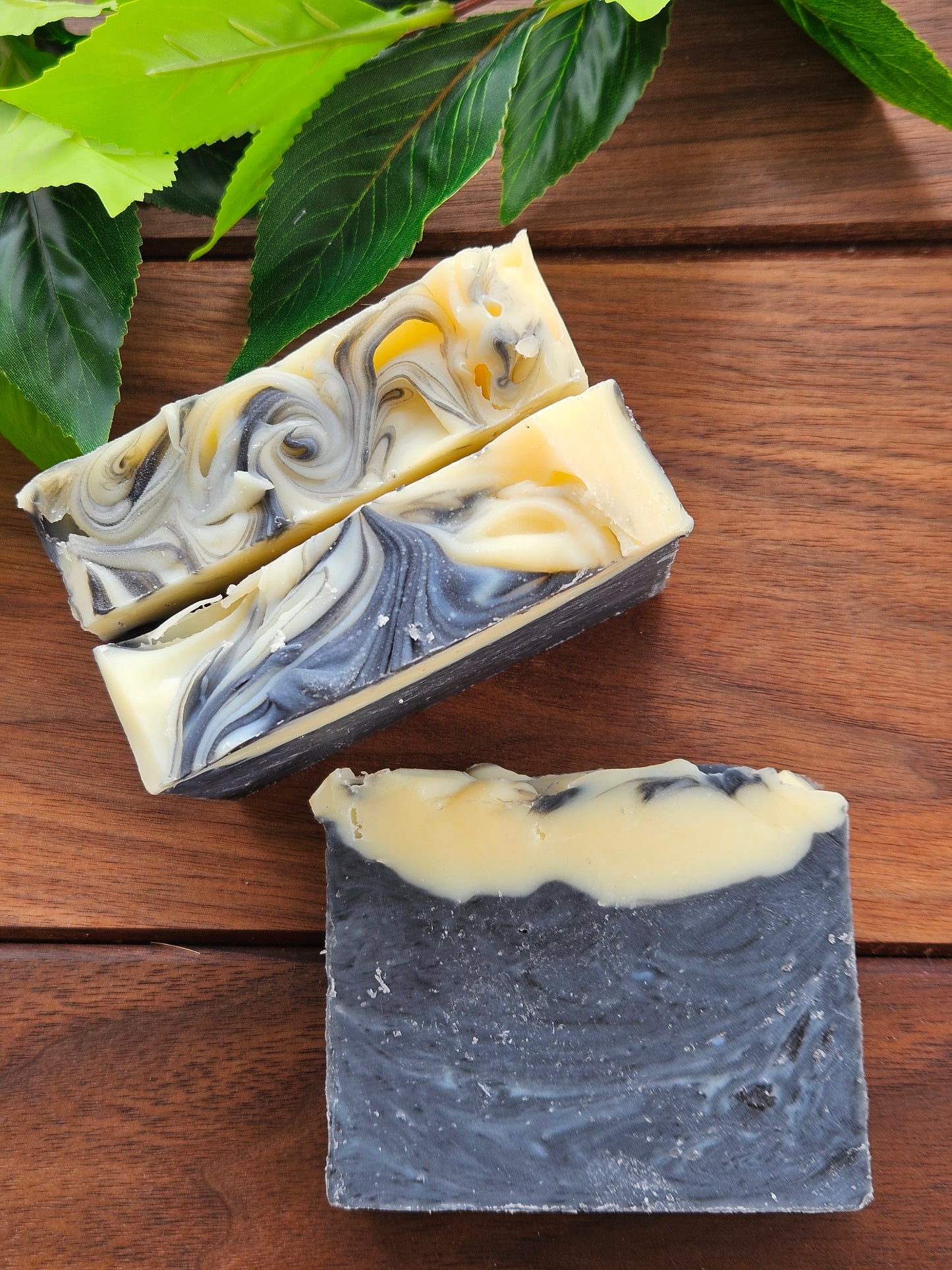 Three bars of soap with marbled patterns on a wooden surface, surrounded by green leaves.