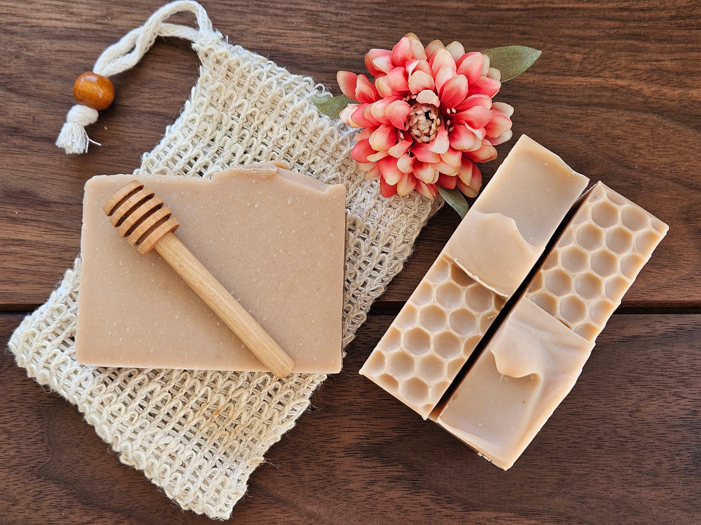 Beige soap bars with honeycomb design, a wooden honey dipper, and a pink flower on a textured surface.