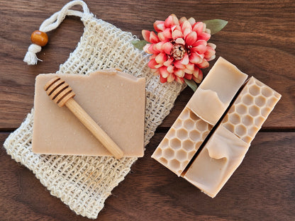 Beige soap bars with honeycomb design, a wooden honey dipper, and a pink flower on a textured surface.