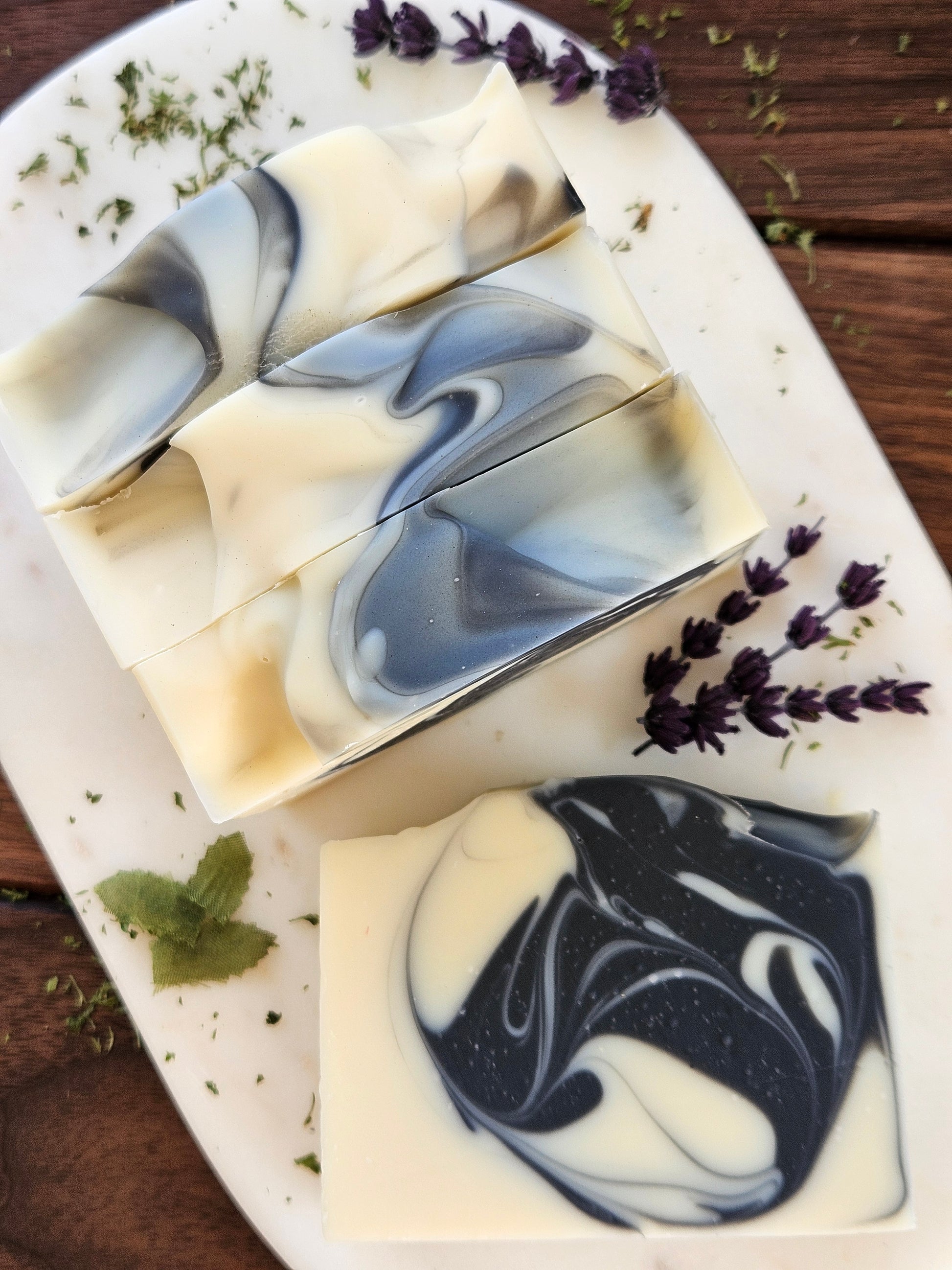 Four bars of marbled soap on a white plate with lavender and mint leaves.
