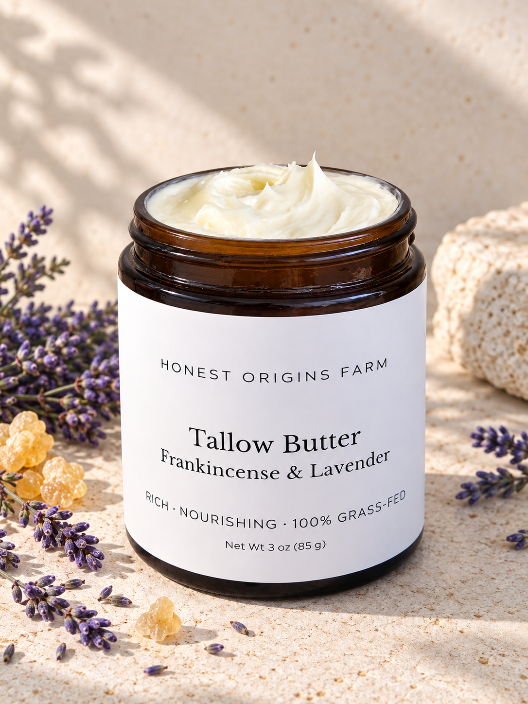 A jar of Honest Origins Farm Tallow Butter in Frankincense & Lavender scent, displayed on a textured beige stone surface with lavender sprigs and light stone props.