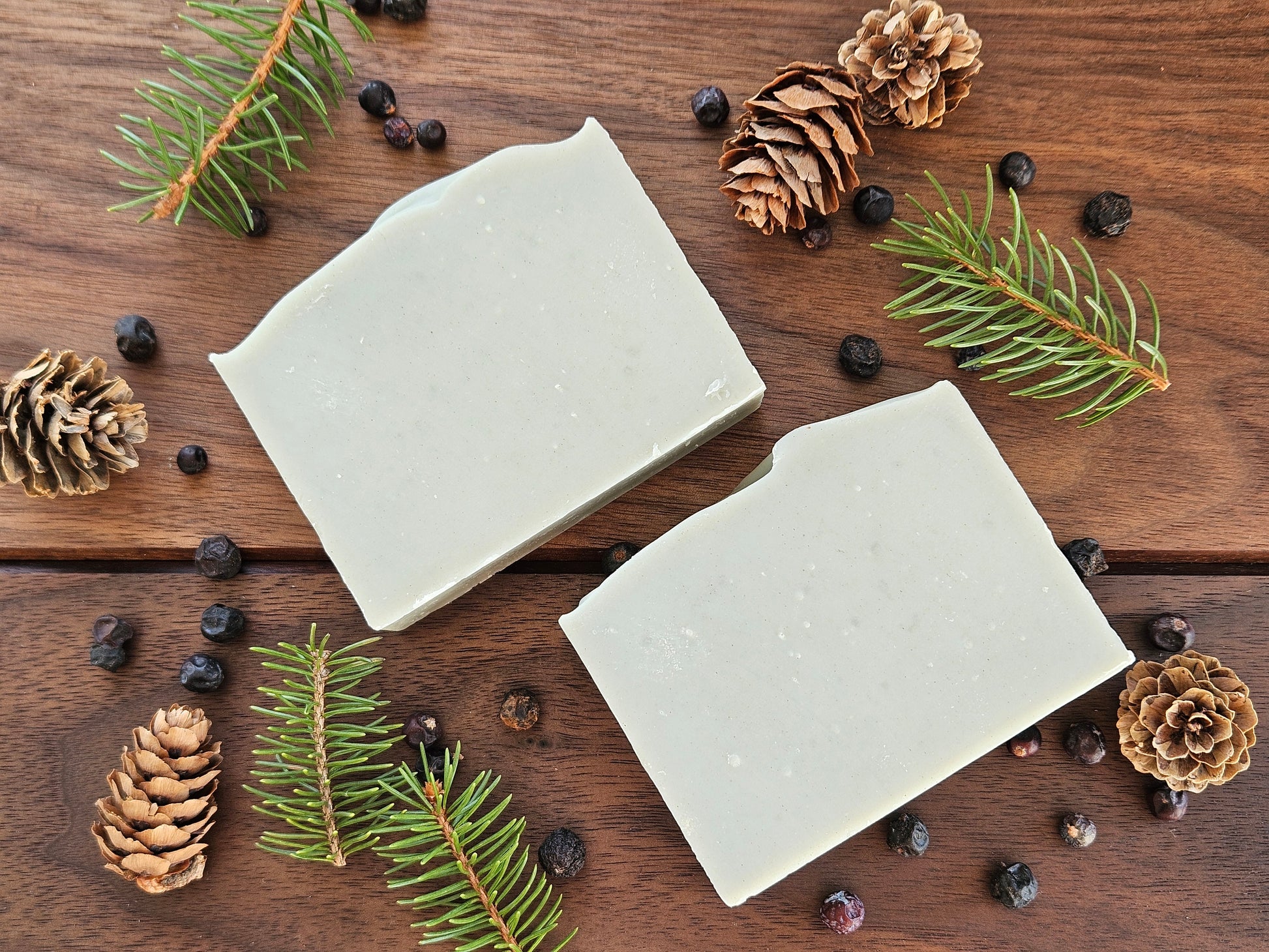 Juniper and Evergreen handmade soap bars on a wooden surface with pinecones and juniper berries and some pine branches