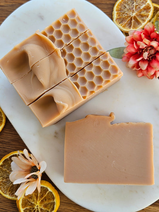 Three bars of soap with honeycomb pattern on a marble slab with decorative flowers and lemons.