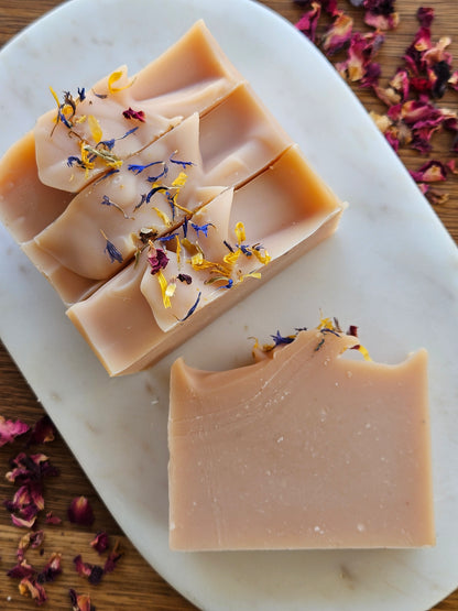 Two bars of soap with floral petals on a white plate, surrounded by dried flowers.