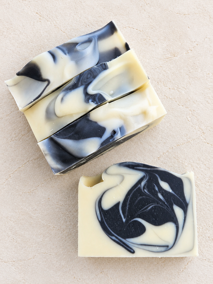 Four rectangular bars of marbled soap with a cream and black swirl pattern, arranged on a light beige textured surface.