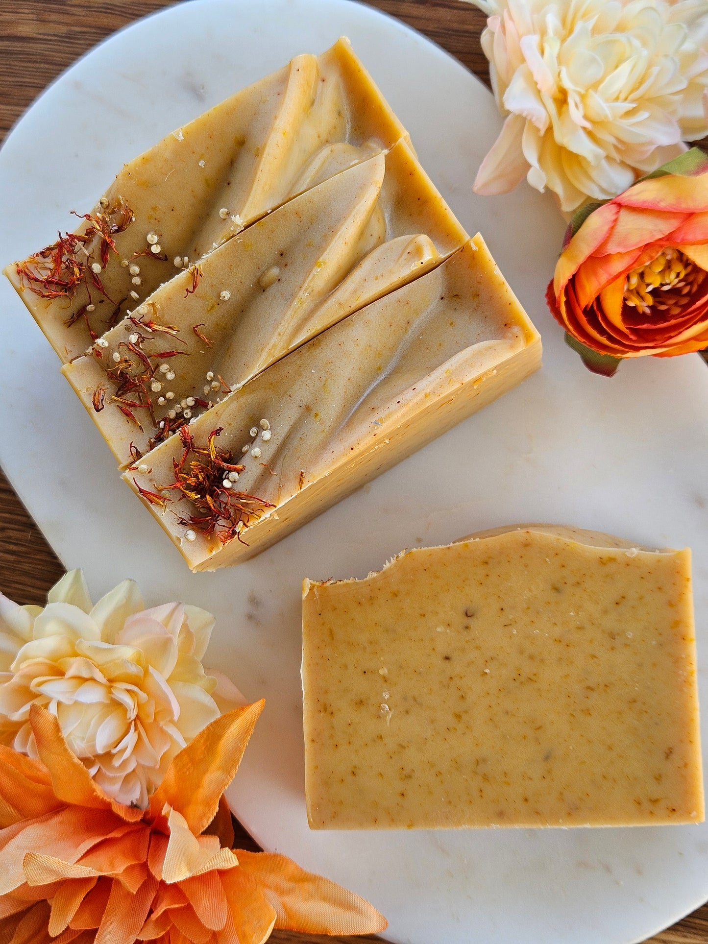 Two bars of soap with visible ingredients on a white plate surrounded by flowers.