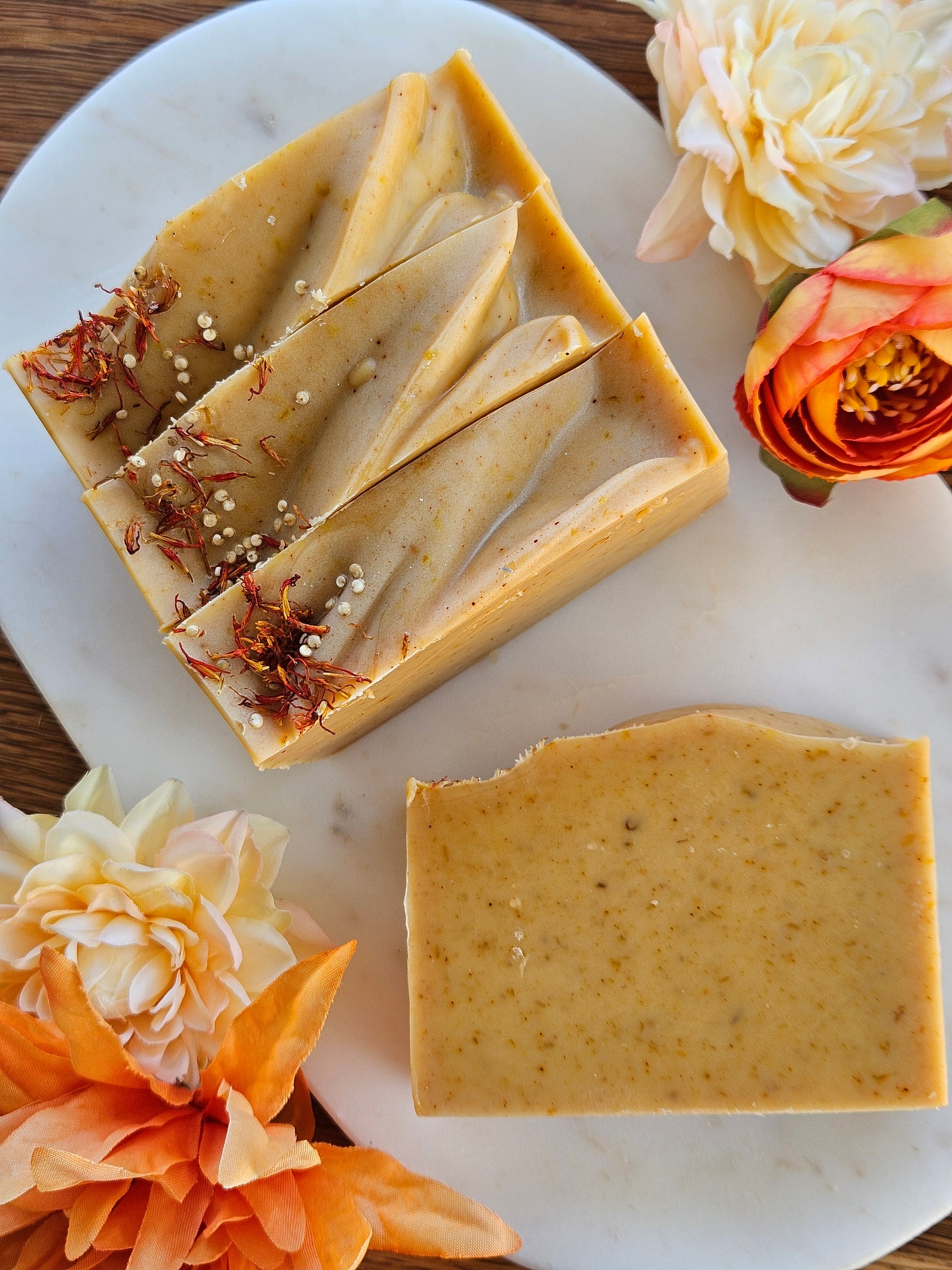 Two bars of soap with visible ingredients on a white plate surrounded by flowers.