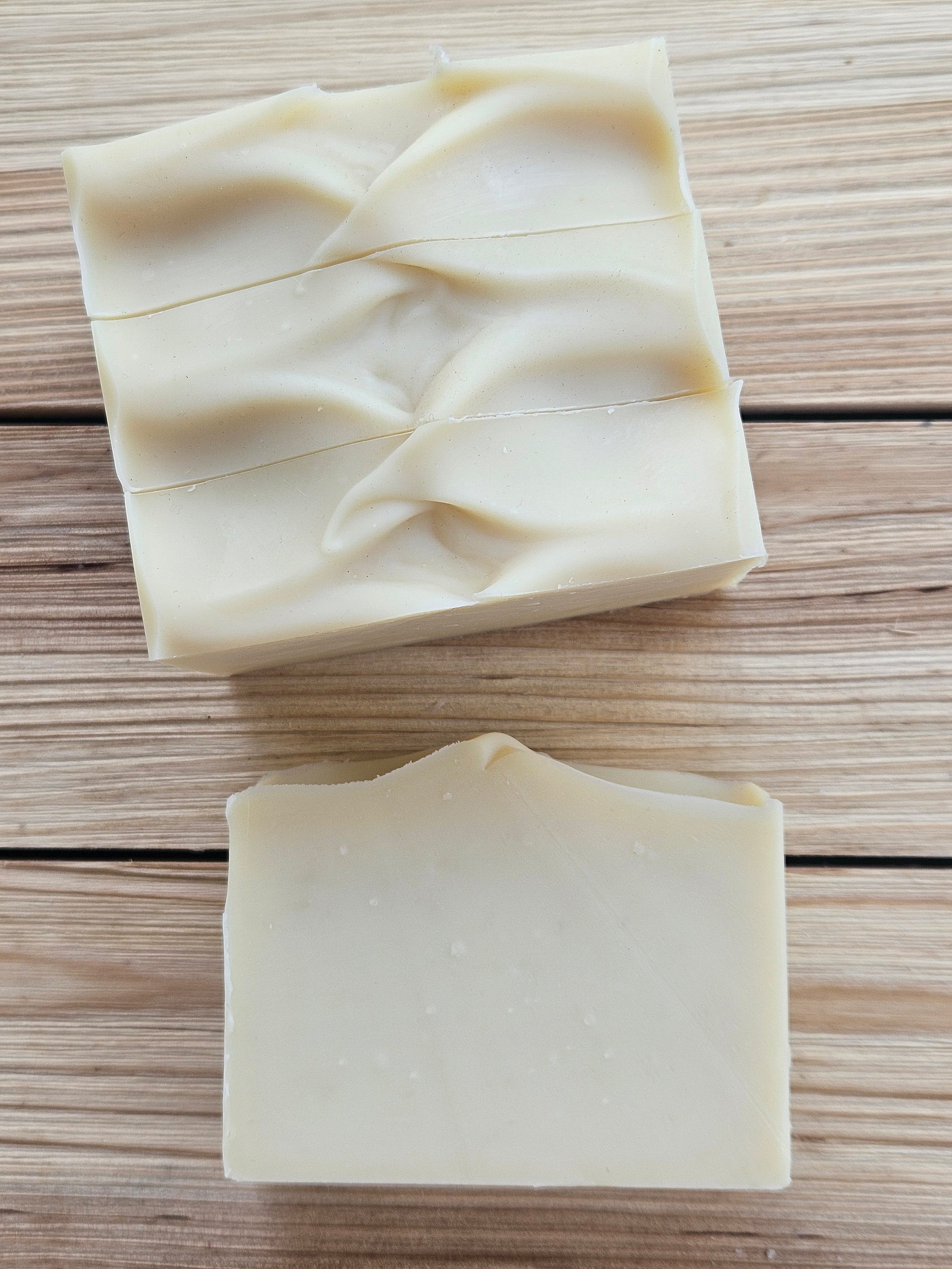 Four rectangular bars of pale cream-colored handmade soap with swirled tops, displayed on a light brown wooden plank background.