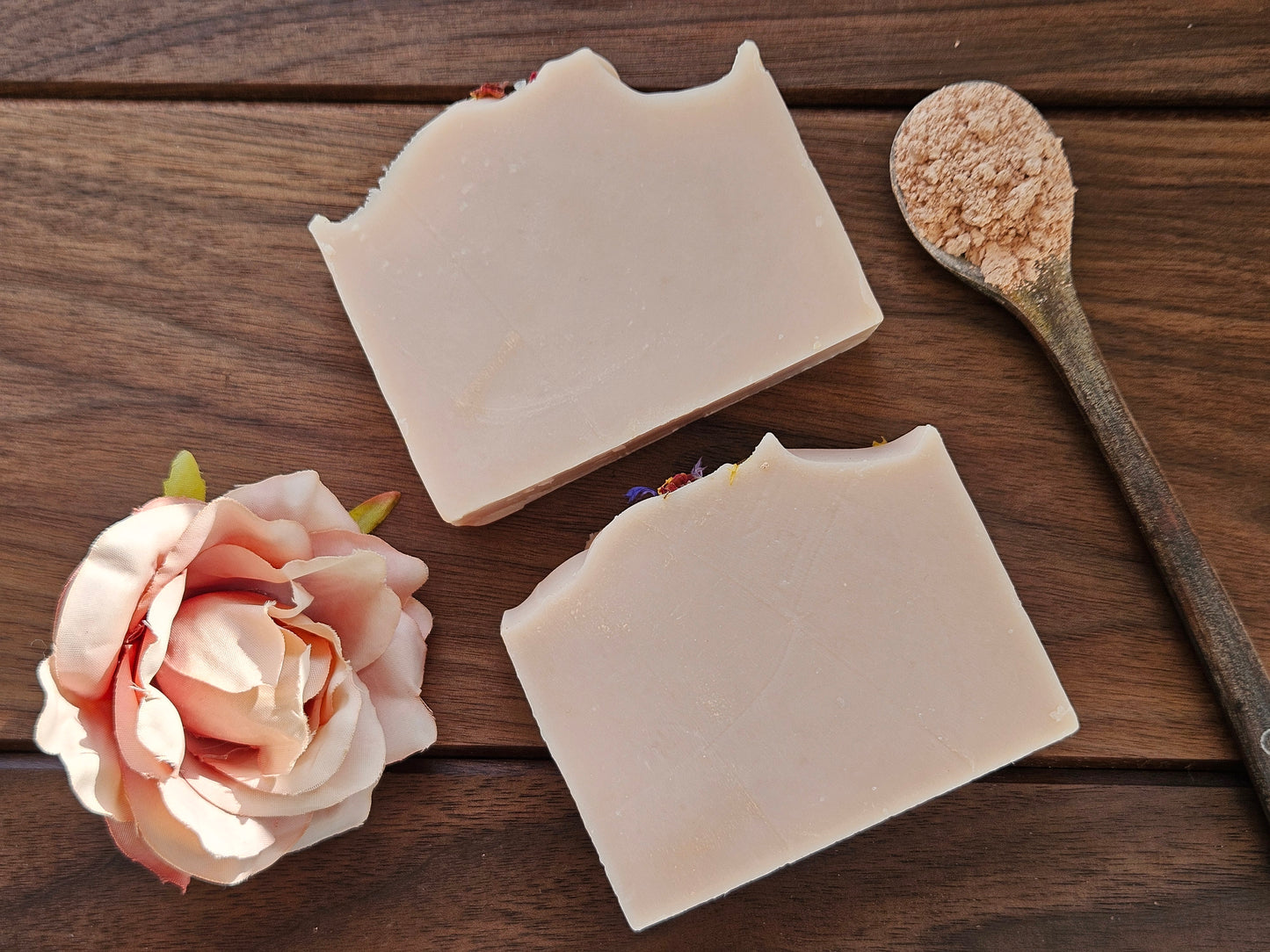 Wildflower Rose soap bars on a wooden surface with a rose and a spoon of pink clay
