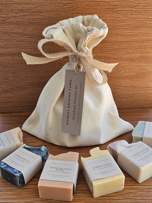 Collection of soap bars with a drawstring bag on a wooden surface, featuring 'Honest Origins & Farm' branding.