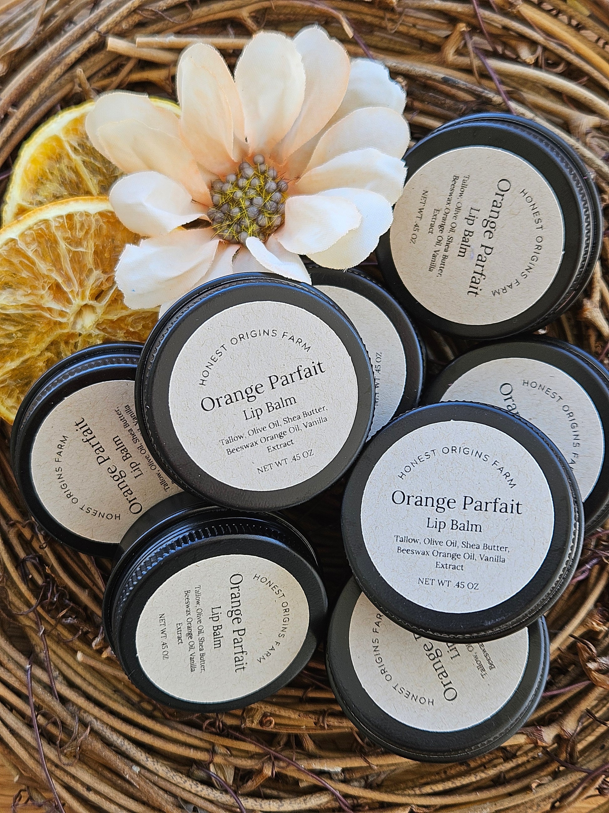Orange Parfait lip balm containers on a woven surface with a flower and orange slice.