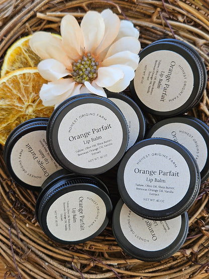 Orange Parfait lip balm containers on a woven surface with a flower and orange slice.