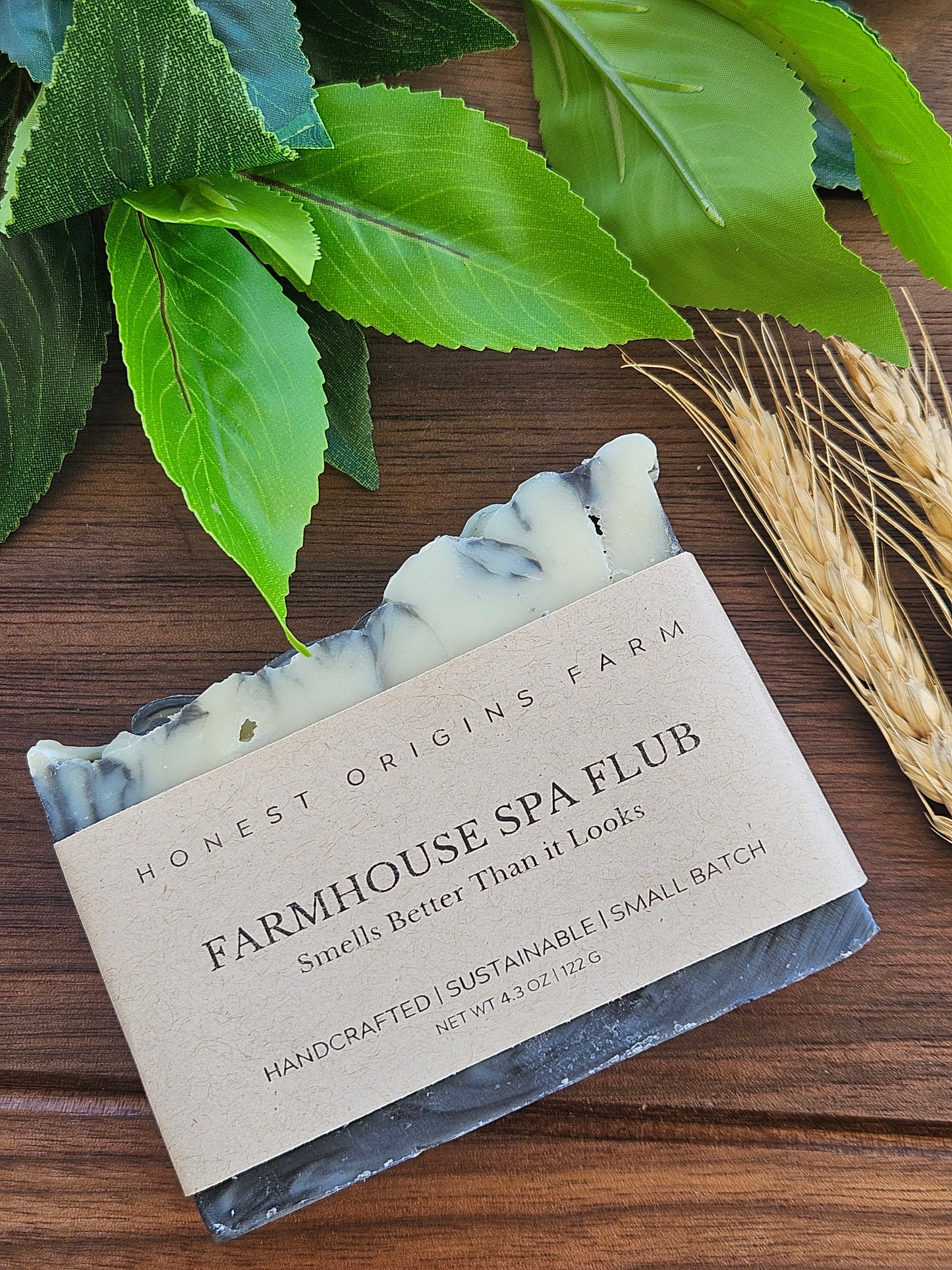 Bar of soap with a label on a wooden surface with leaves and wheat stalks.