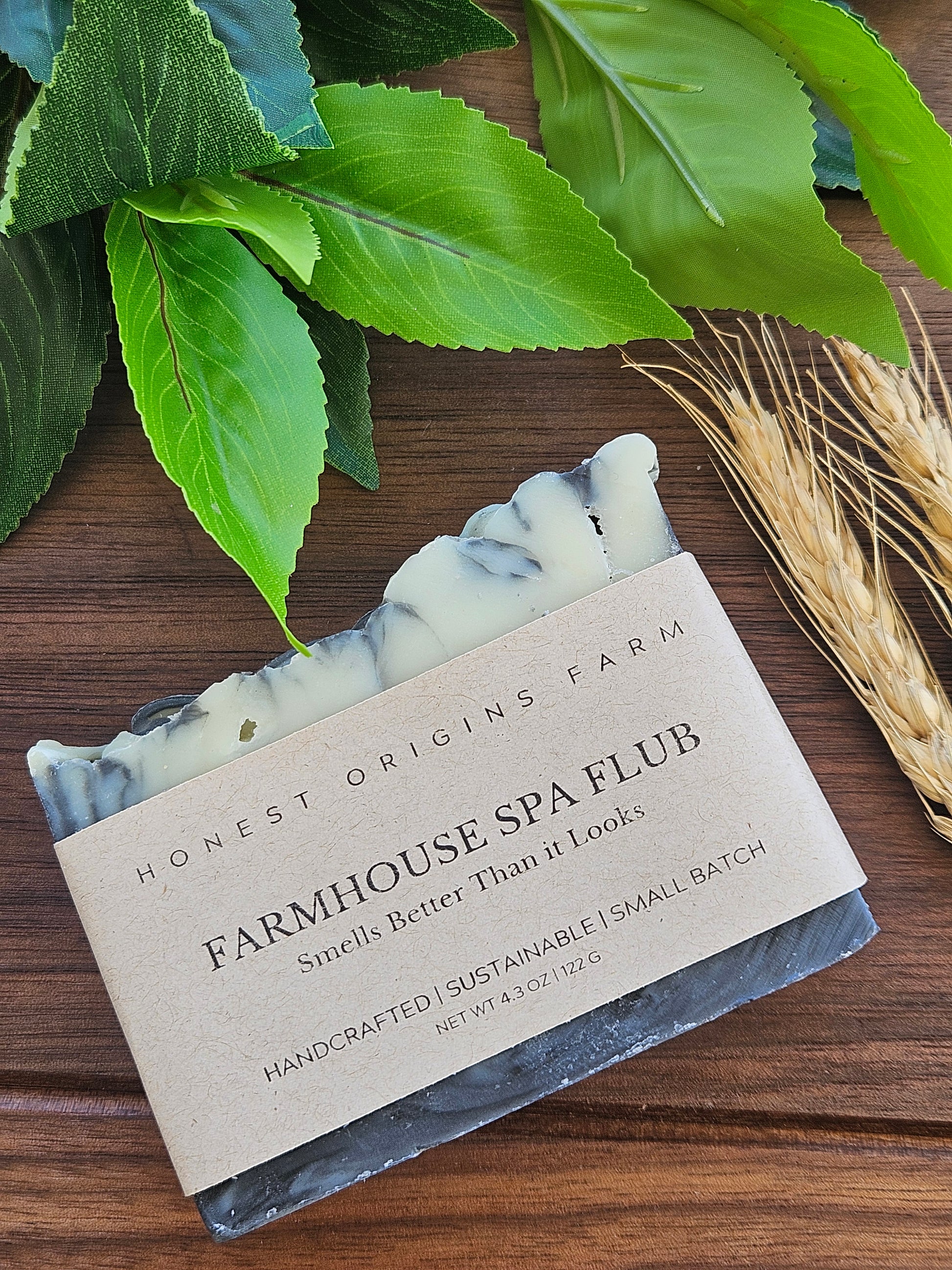 Bar of soap with a label on a wooden surface with leaves and wheat stalks.