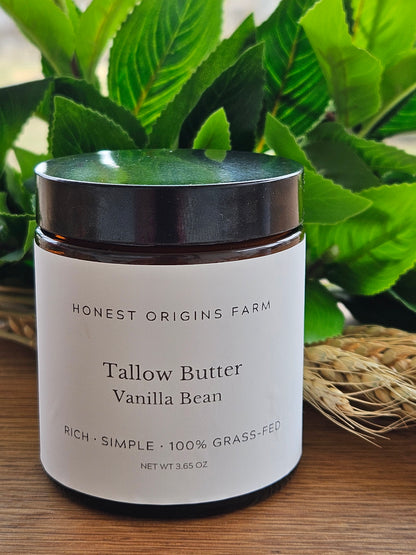 Jar of tallow butter with vanilla bean flavor on a wooden surface with green leaves in the background