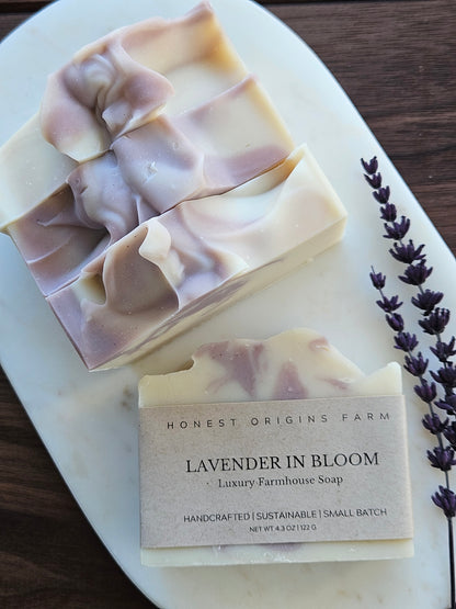 Four bars of soap on a white plate with lavender flowers, one bar is wrapped and the other is unwrapped.