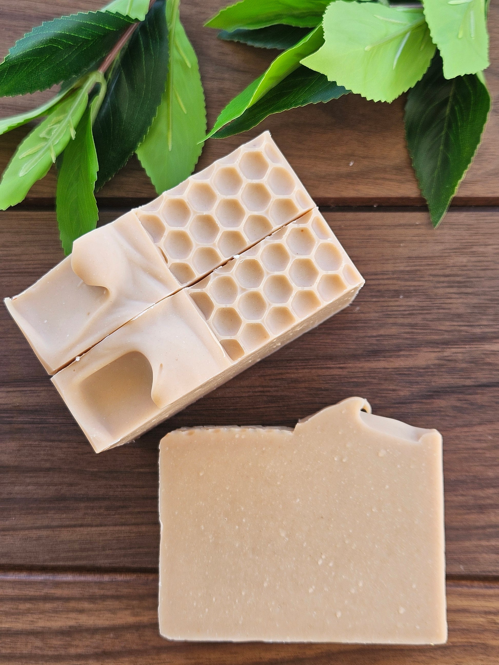 Beige soap bar with honeycomb design on a wooden surface with green leaves.