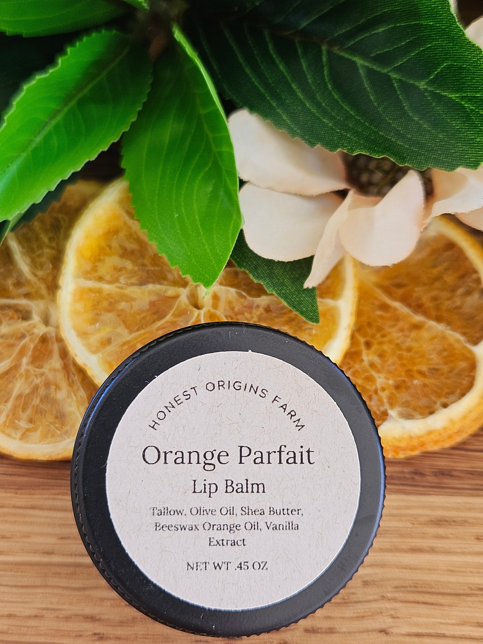Orange Parfait lip balm with oranges and leaves on a wooden surface