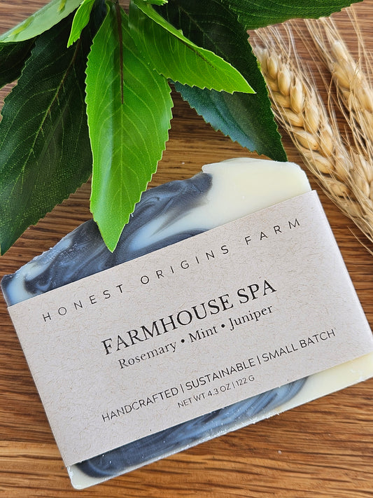 Bar of soap with a label on a wooden surface with leaves and wheat stalks.